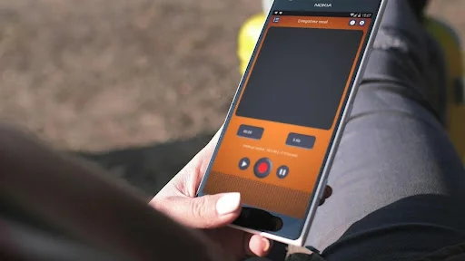 Hand holding smartphone with Voice Memo audio recorder displaying orange interface for recording and playing back voice memos